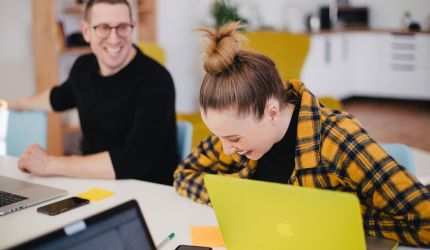 Ein Mitarbeiter und eine Mitarbeiterin erfreuen sich bei der Arbeit am Laptop
