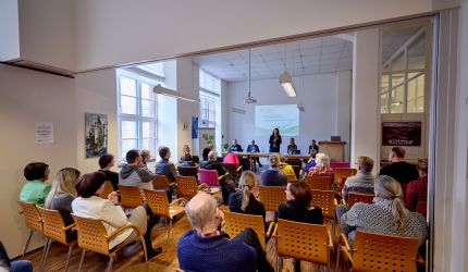 Gaeste sitzen in Reihen im Vortragsraum 