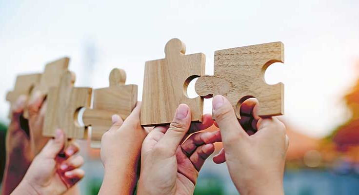Vier Hände halten einzelne Puzzleteile in die Höhe