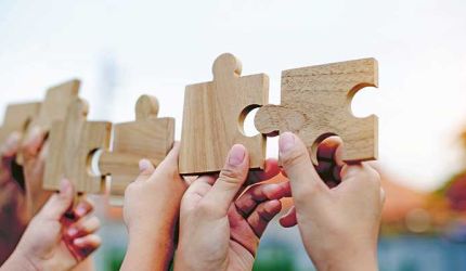 Vier Hände halten einzelne Puzzleteile in die Höhe