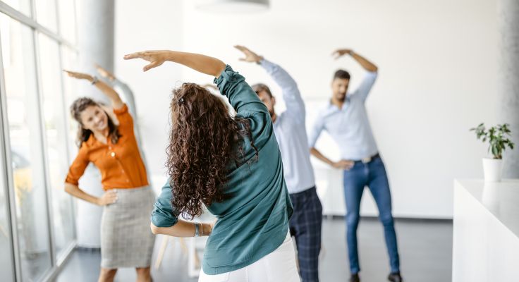 Gruppe von Kollegen in einem hellen Raum, die gemeinsam Dehnübungen machen