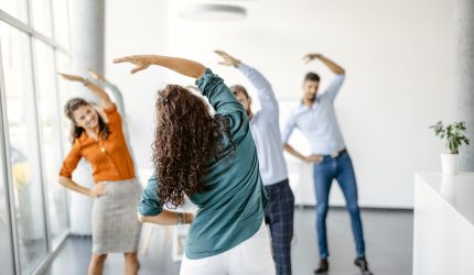 Gruppe von Kollegen in einem hellen Raum, die gemeinsam Dehnübungen machen