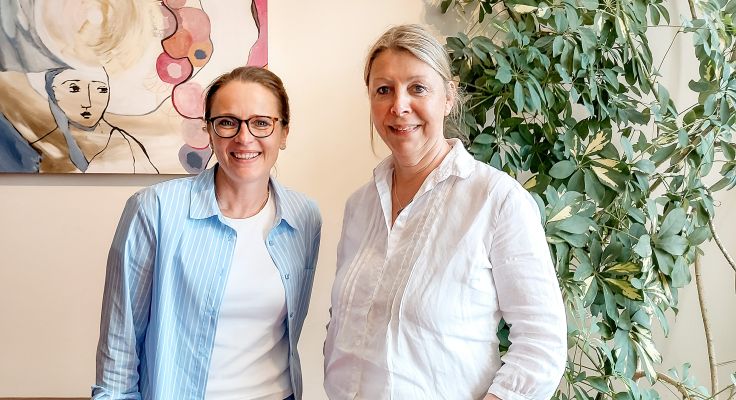 Miriam Jorke und Britta Buchholz stehen vor Kunstbild und Grünpflanze