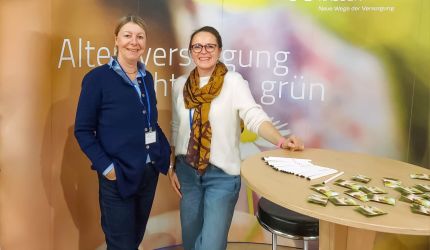 Britta Buchholz und Miriam Jorke stehen vor dem Messestand