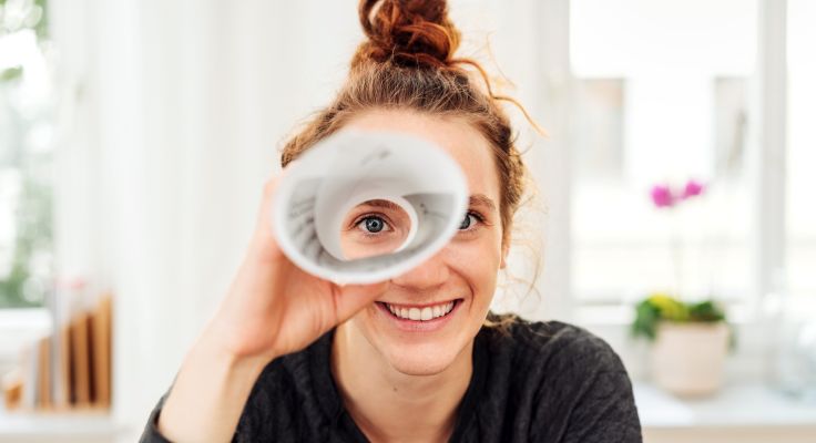 Eine Frau, die durch ein aufgerolltes Stück Papier schaut